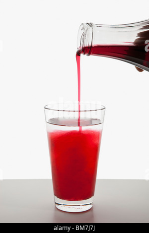 Dettaglio di sciroppo di frutta che viene versato in un bicchiere di acqua Foto Stock