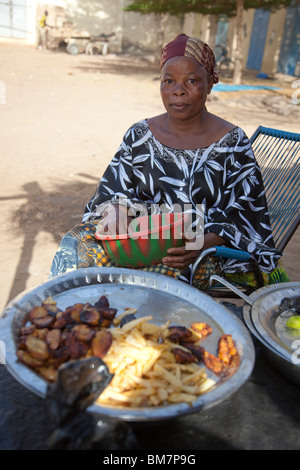 Una donna vende la frittura di banane da cuocere (alloco) e patate per la colazione vicino alla stazione degli autobus di Segou, Mali. Foto Stock