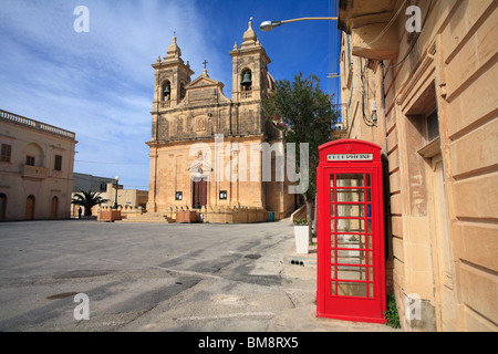 Un rosso British telefono box si siede da solo in una piazza vuota in un ambiente mediterraneo in un villaggio sull'isola di Gozo, Malta Foto Stock