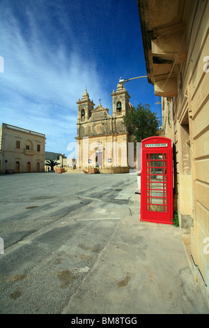 Un rosso British telefono box si siede da solo in una piazza vuota in un ambiente mediterraneo in un villaggio sull'isola di Gozo, Malta Foto Stock