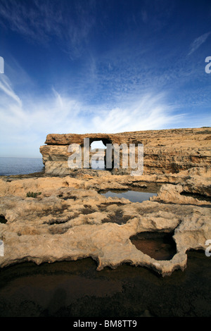 Un cielo blu con striature bianche nuvole dietro la finestra azzurra, una funzione di calcare sulla costa occidentale di Gozo Foto Stock
