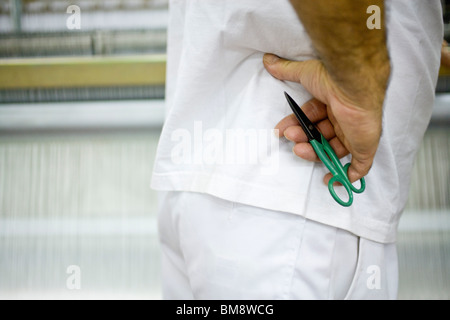 Macchinista in piedi accanto al telaio di tessitura, tenendo in mano un paio di forbici Foto Stock