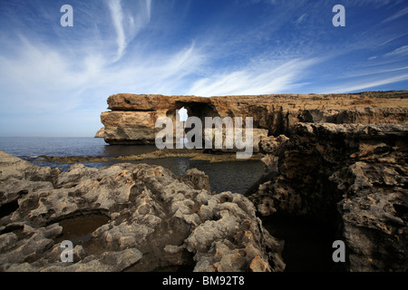 Un cielo blu con striature bianche nuvole dietro la finestra azzurra, una funzione di calcare sulla costa occidentale di Gozo Foto Stock