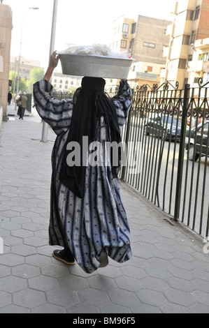 Lady egiziana che trasportano gli spuntini di vendere al di fuori di al-Azhar moschea, il Cairo islamico, Egitto , Foto Stock