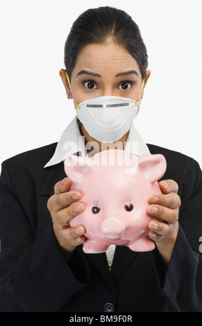 Imprenditrice indossando un H1N1 di maschera e tenendo un salvadanaio Foto Stock