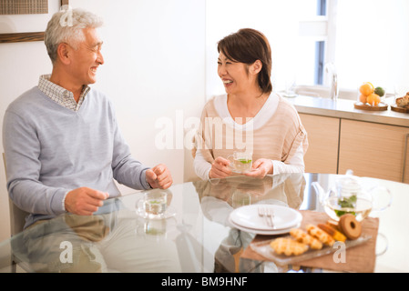 Coppia senior bere il tè al tavolo da pranzo, sorridente Foto Stock