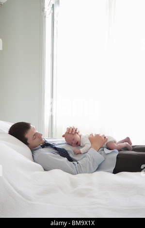 Padre di lavoro risiede con due settimana neonato sul letto Foto Stock