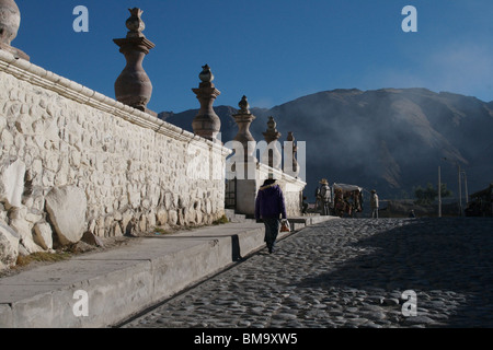 Donna che cammina al fianco di chiesa parete vicino Canyon del Colca, Perù Foto Stock
