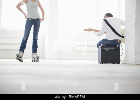 Donna su pattini a rotelle e uomo seduto sulla riproduzione di amp per chitarra elettrica Foto Stock