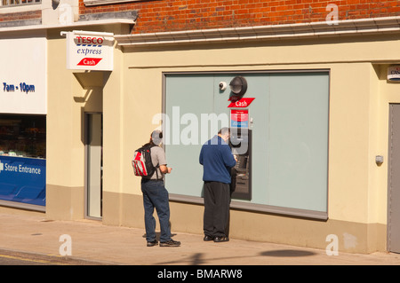 La gente ottenere contanti da un supermercato Tesco Express speedbank atm in Norwich , Norfolk , in Inghilterra , Gran Bretagna , Regno Unito Foto Stock