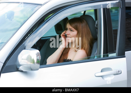 Giovane donna al telefono seduto in un'auto. Foto Stock