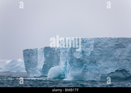 Grande oceano onda schiantarsi contro il gigante blu alti iceberg erodendo l'enorme bergs Mare di Weddell off Oceano Meridionale Antartide sotto il cielo nuvoloso Foto Stock