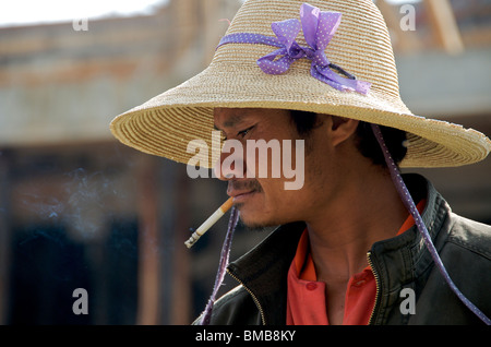 Commerciante nel cappello di paglia godendo di una sigaretta la sagomatura del mercato Cina Yunnan Foto Stock