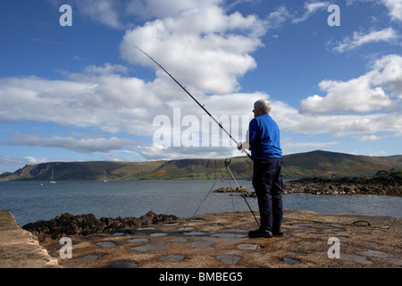 Uomo di mezza età di pesca con asta e la linea del County Antrim coast Irlanda del Nord Regno Unito Foto Stock