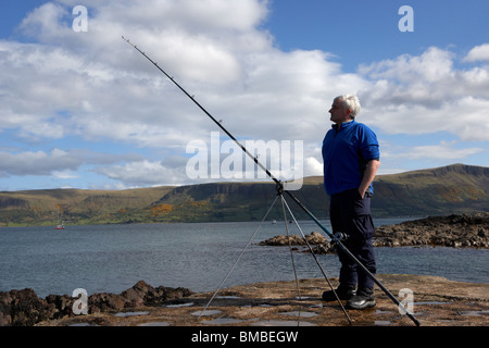 Uomo di mezza età di pesca con asta e la linea del County Antrim coast Irlanda del Nord Regno Unito Foto Stock