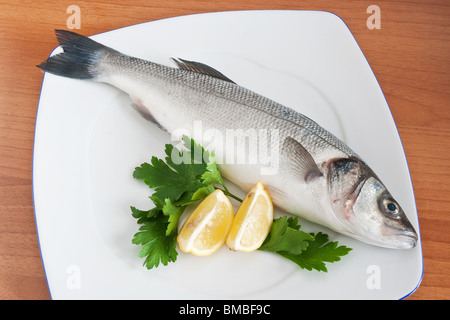 Piastra con la spigola, limone e prezzemolo isolato su sfondo di legno Foto Stock