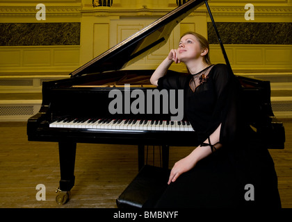 Ragazza vestiti di nero si siede vicino ad un pianoforte e dreamily guarda in alto Foto Stock