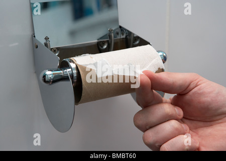 mano di mans tirando l'ultimo foglio rimanente di carta igienica su un'emergenza di porta rotolo di carta igienica fuori dalla crisi rotolo di bobina di gabinetto Foto Stock