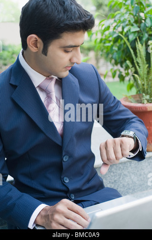 Imprenditore usando un computer portatile e guardando il suo orologio da polso Foto Stock