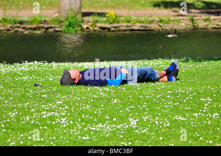 Uomo di dormire sulla banca erbosa del fiume nel Parco Foto Stock