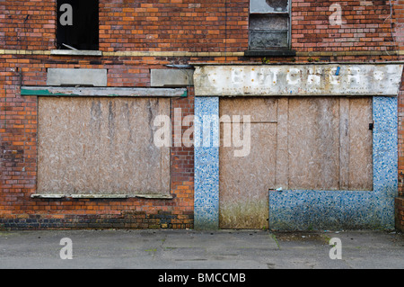 Abbandonato il negozio con bloccato in alto le finestre e le porte in una strada a Belfast Foto Stock