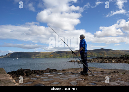 Uomo di mezza età di pesca con asta e la linea del County Antrim coast Irlanda del Nord Regno Unito Foto Stock