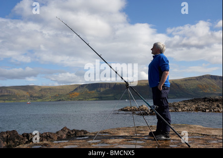 Uomo di mezza età di pesca con asta e la linea del County Antrim coast Irlanda del Nord Regno Unito Foto Stock