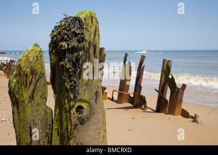 Montanti in legno e ritorto metallo arrugginito lungo Happisburgh seashore, Norfolk. Foto Stock