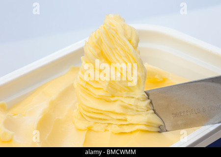 Coltello raccogliendo da spalmare grasso lattiero da spalmare in una vasca di plastica contenitore Foto Stock