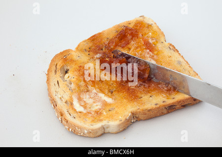Diffusione di marmellata su una fetta di pane tostato con burro fuso usando un coltello Foto Stock