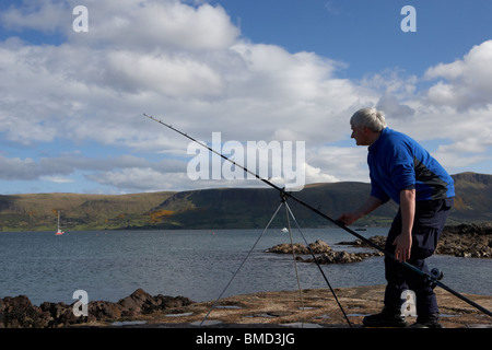 Uomo di mezza età di pesca con asta e la linea del County Antrim coast Irlanda del Nord Regno Unito Foto Stock