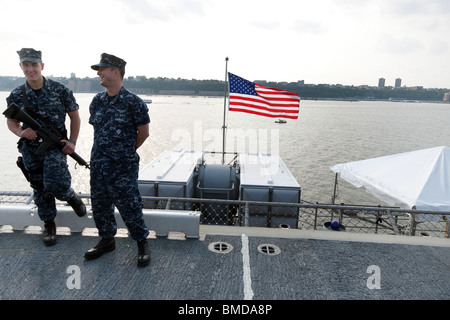 Bandiera americana vola da poppa di portaerei Iwo Jima come marinaio di guardia sorrisi con buddy durante la settimana della flotta di New York City Foto Stock