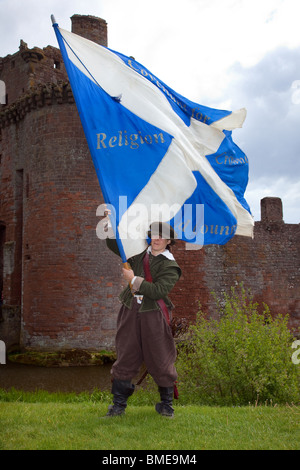 Donna portabandiera Covenantar che sventolava la grande bandiera scozzese dei covenanti al castello di Caerlaverock, storica fortezza medievale, Dumfries, Scozia, Regno Unito Foto Stock