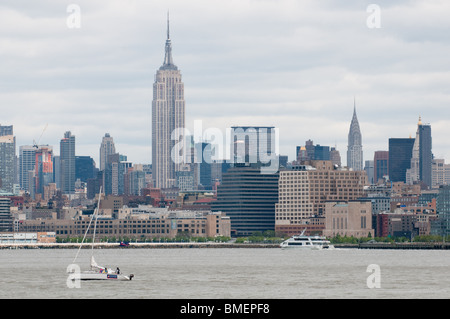 Piccola imbarcazione a vela con Empire State building e lo skyline di Manhattan in background, New York City, NY, STATI UNITI D'AMERICA. Foto Stock