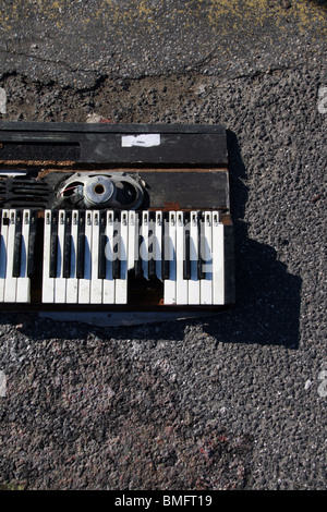 Vecchio sintetizzatore musicale pianoforte danneggiato in strada Foto Stock