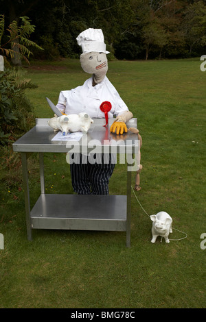 Macellaio con maiali e salsicce che producono un coltello al Bisterne Annual Scarecrow Festival, bisterne, New Forest National Park, Hampshire, Regno Unito nel mese di settembre Foto Stock