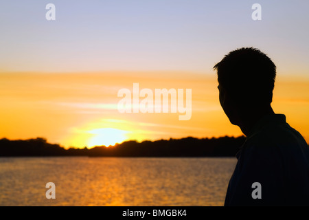 Willmar, Minnesota, Stati Uniti d'America; silhouette di un uomo guardando il tramonto su un lago Foto Stock