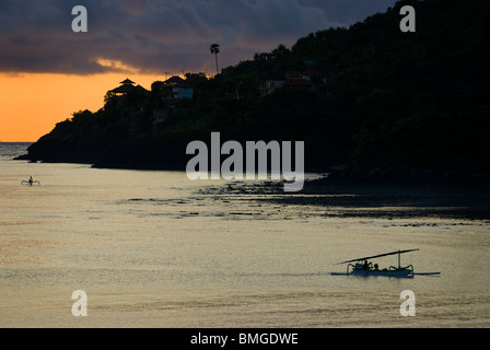 Come il sole sorge su Amed, Bali, pescatori nelle loro piccole imbarcazioni chiamato jukung rientro a riva a sbarcare le loro catture di giorno in giorno. Foto Stock