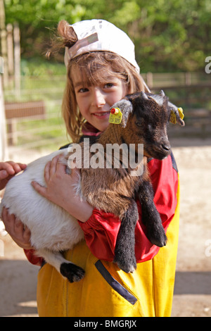 Giovane ragazza tenendo un giovane capra nelle sue braccia a uno zoo di animali domestici Foto Stock