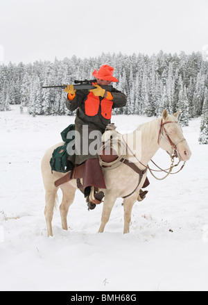 Cacciatore dei cervi riding del cavallo bianco neve nel fucile di puntamento Foto Stock