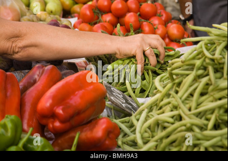 Un stalholder la raccolta a mano i fagiolini da un mercato stail piena di fagioli, peperoni, pomodori, asparagi e altri frutti. Foto Stock