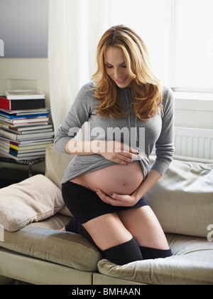 Donna incinta sul divano ventre di contenimento Foto Stock