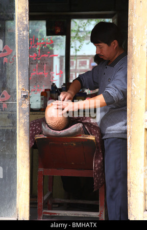 L'uomo avente una rasatura in un negozio di barbiere di Kashgar, occidentale provincia dello Xinjiang, Cina. Foto Stock