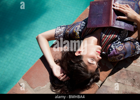 Donna giacente presso la piscina con un libro Foto Stock