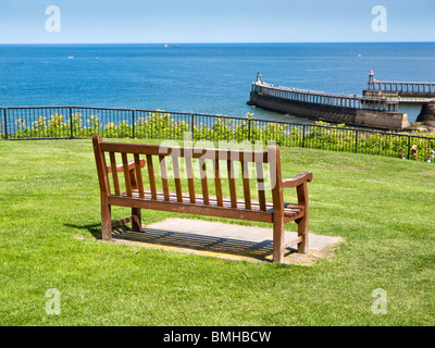 Una panchina nel parco che si affaccia sul mare e il molo a Whitby, North Yorkshire, Inghilterra, Regno Unito Foto Stock