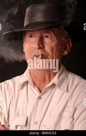 Senior Cowboy di fumare una sigaretta e indossando un cappello da cowboy Foto Stock