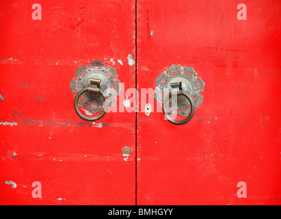 Vecchia porta rossa con bronzo doorknockers che mostrano il cinese taoista di simboli Foto Stock