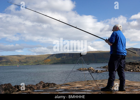 Uomo di mezza età la pesca con asta di linea e di controllo per le punture sulla contea di Antrim coast Irlanda del Nord Regno Unito Foto Stock