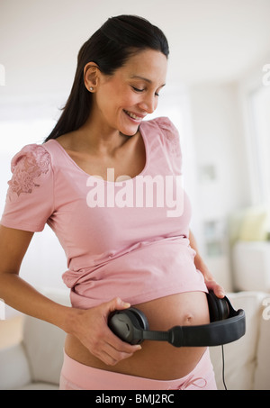 Donna incinta partecipazione delle cuffie sul suo ventre Foto Stock