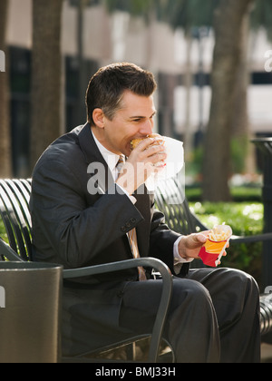 Imprenditore di mangiare il pranzo su una panchina nel parco Foto Stock